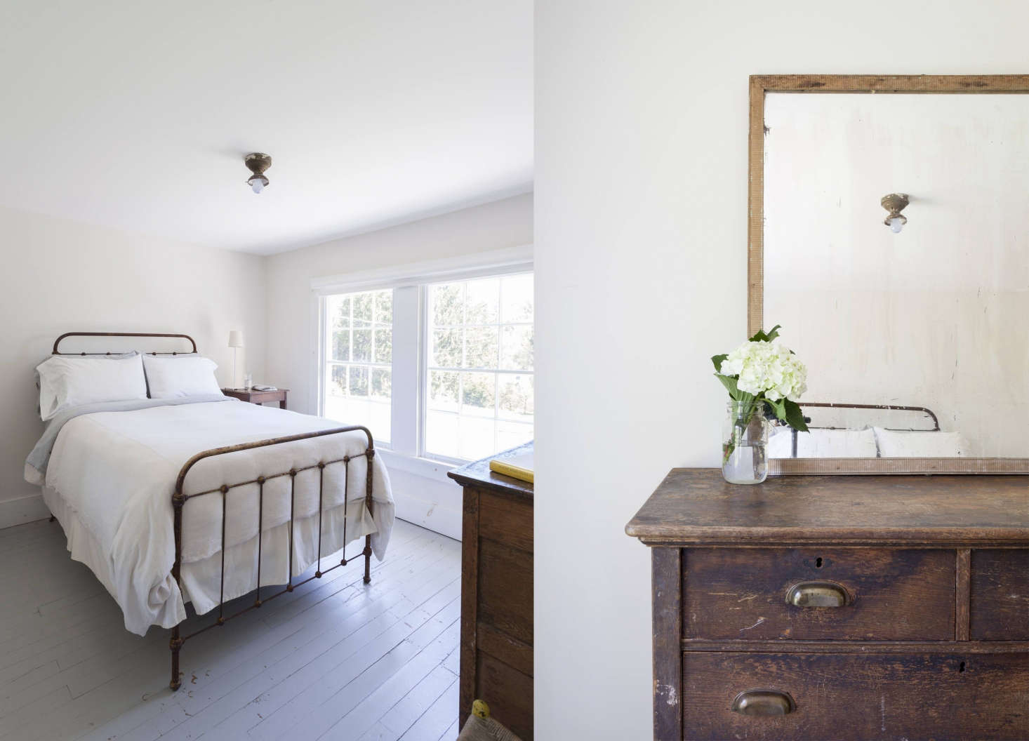 An old cast-iron bed frame and a minimalist layout in a farmhouse bedroom. The windows have their original wavy glass.