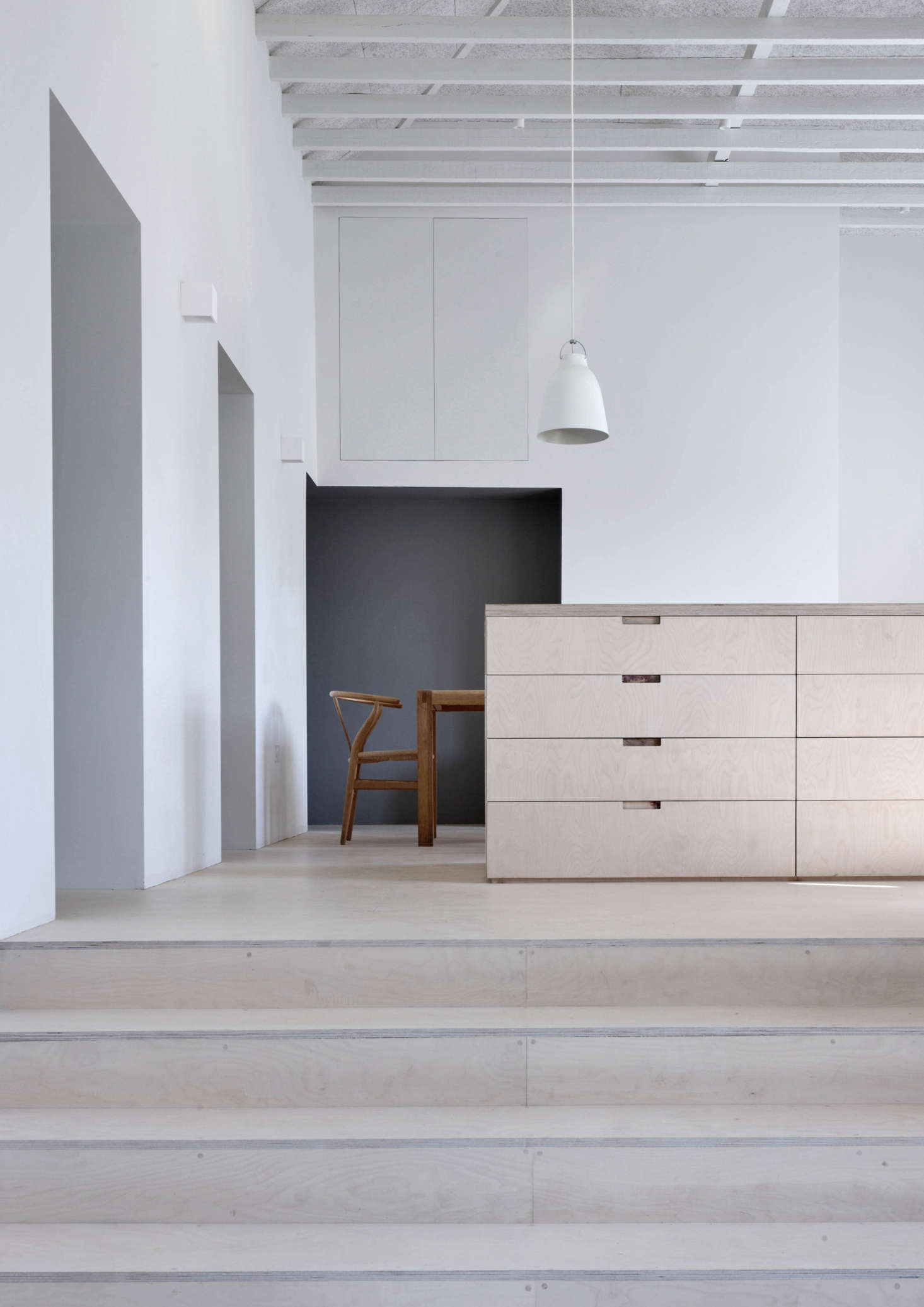 A Caravaggio P3 Pendant Light hangs over the central island, which like the steps, floor, and other cabinets are made of birch plywood finished with a clear matte oil.