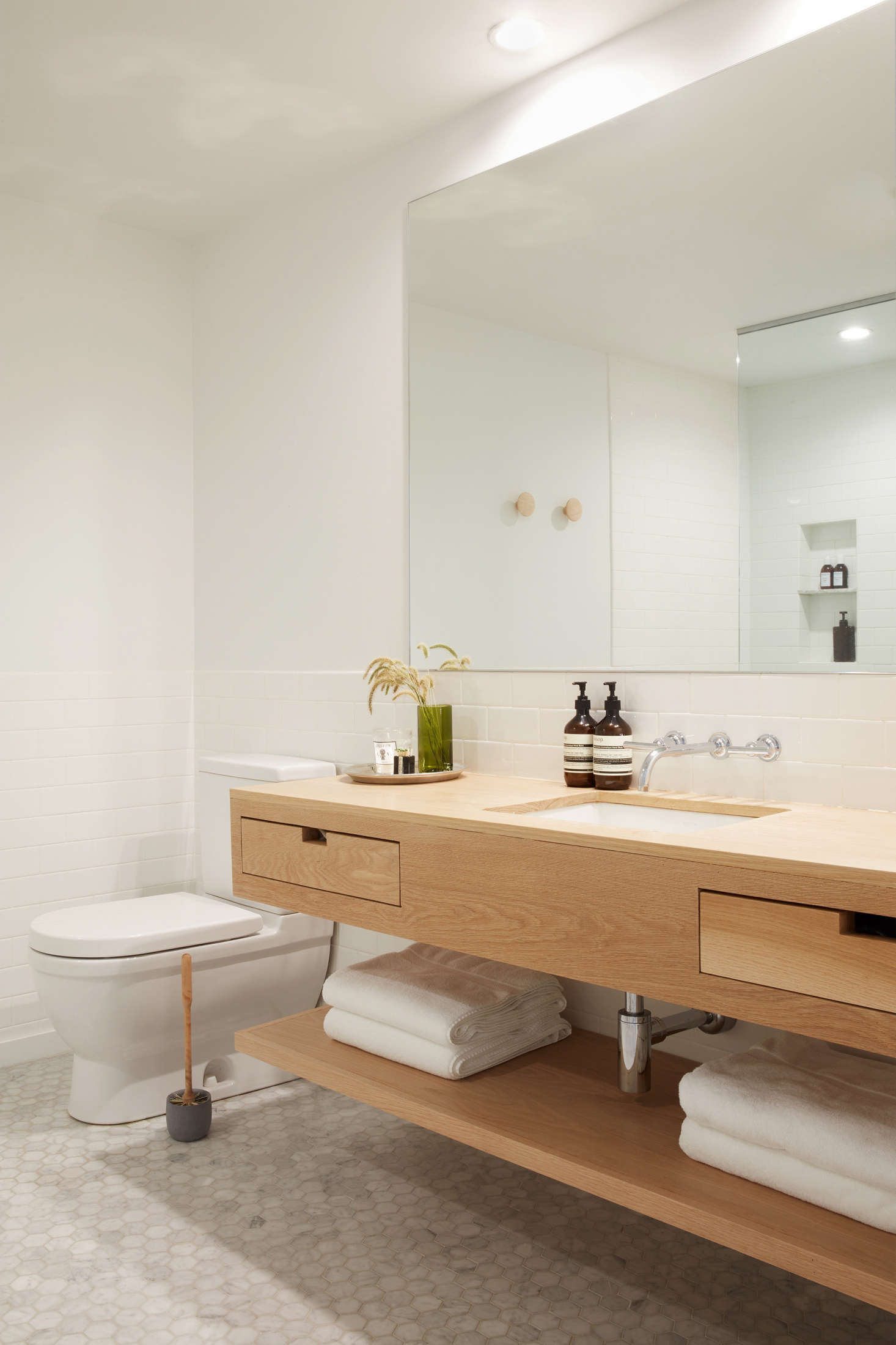 The guest bath is tiled with gray Carrara marble hexagonal tile from Stone Source. The toilet brush and holder are by Iris Hantverk and a green glass vase, from Brooklyn