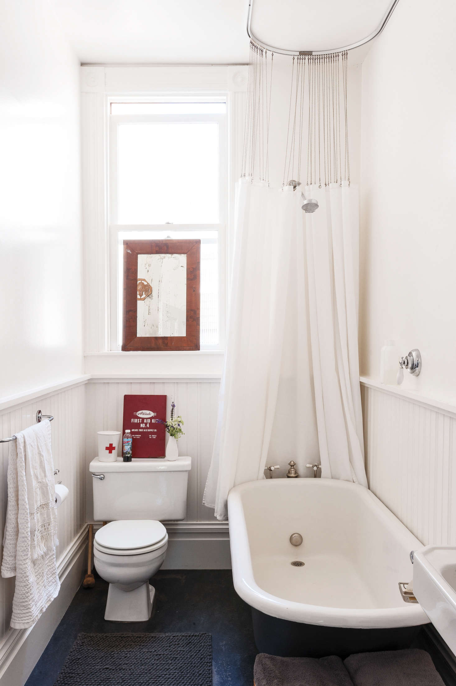 In her wee bath, clothing designer Dagmar Daley ditched her curtains, used all white to maximize the sense of light and air, and she used vertical elements, wainscoting and a shower curtain, to emphasize the height of the room. Photograph by Matthew Williams from Remodelista: A Manual for the Considered Home.
