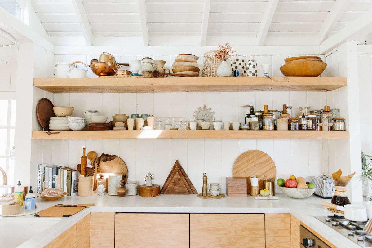 A brass, deck-mounted faucet (just out of frame) and sturdy wood shelving add warmth and a lived-in feel to the whitewashed space.