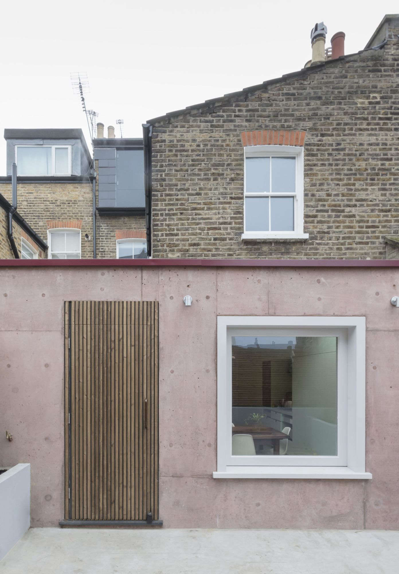 Situated in the back of the house, the six-square-meter (64.5-square-foot) extension features a pigmented cast concrete wall with a slatted wood door and integrated sliding glass window. The new courtyard—shown pre-plantings (it