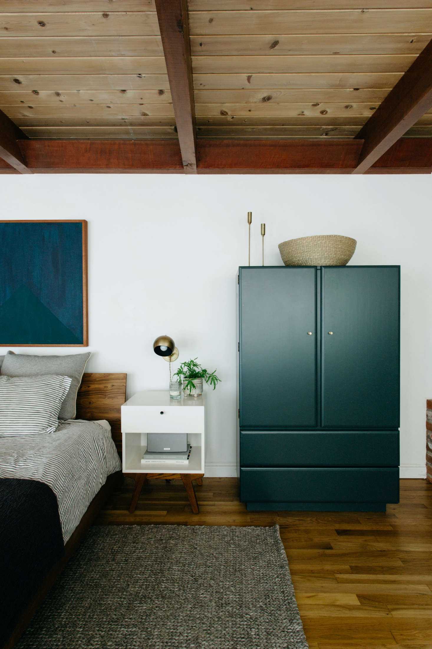 Nye had a vintage armoire refinished in Dark Pewter by Benjamin Moore with subtle brass hardware from Schoolhouse Electric. The dark blue painting above the bed is Courtney Nye