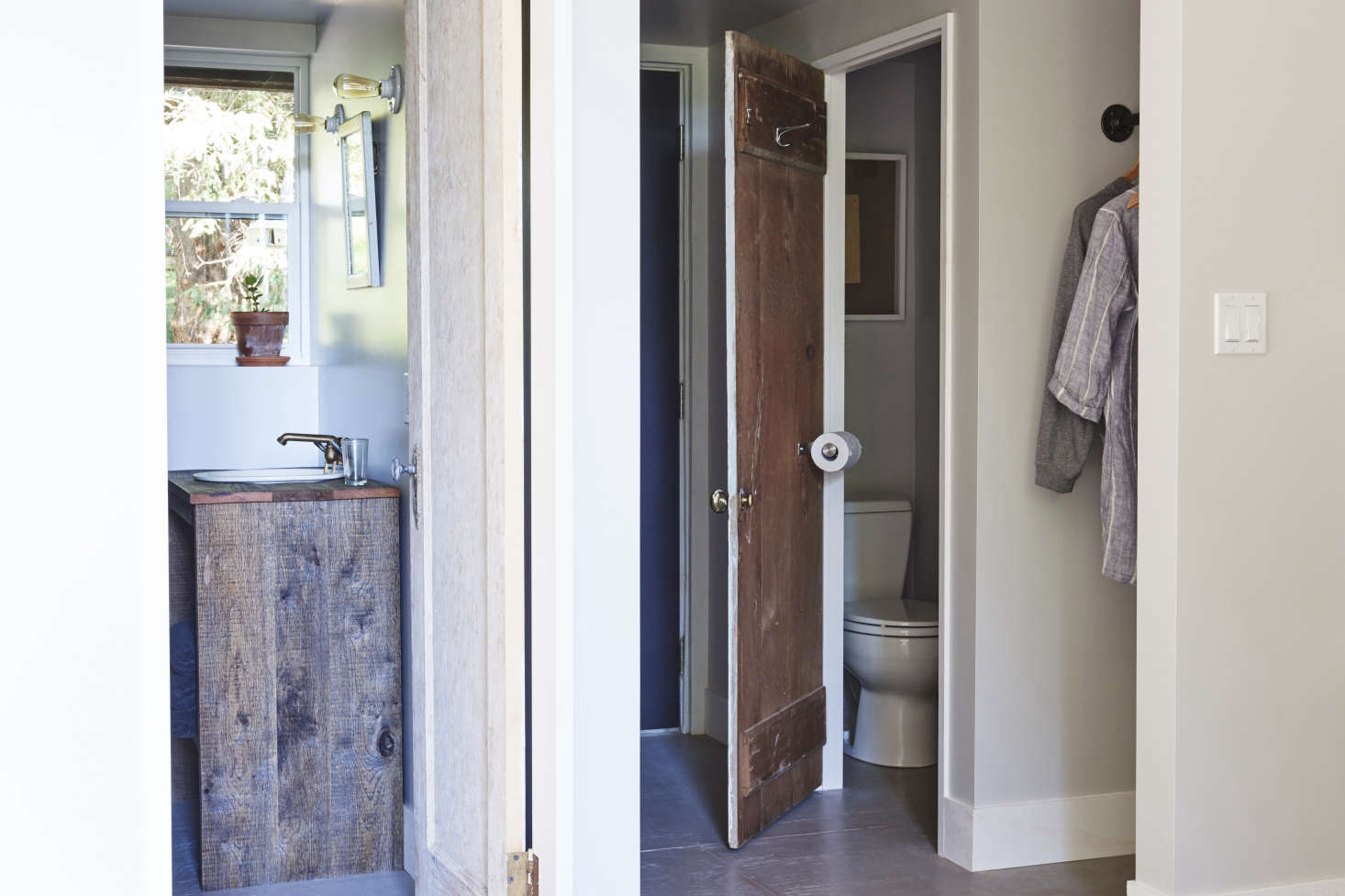 The bathroom suite with a reclaimed-wood vanity. In the WC, a space-saving hack: a toilet-paper holder affixed to the door.