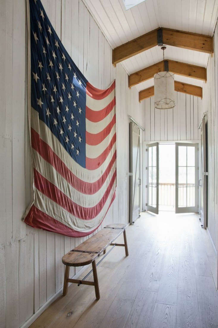 In the hallway of this white painted barn, a vintage American flag provides a bit of color as well as a welcome horizontal element. Photograph from Rachel Halvorson Designs.