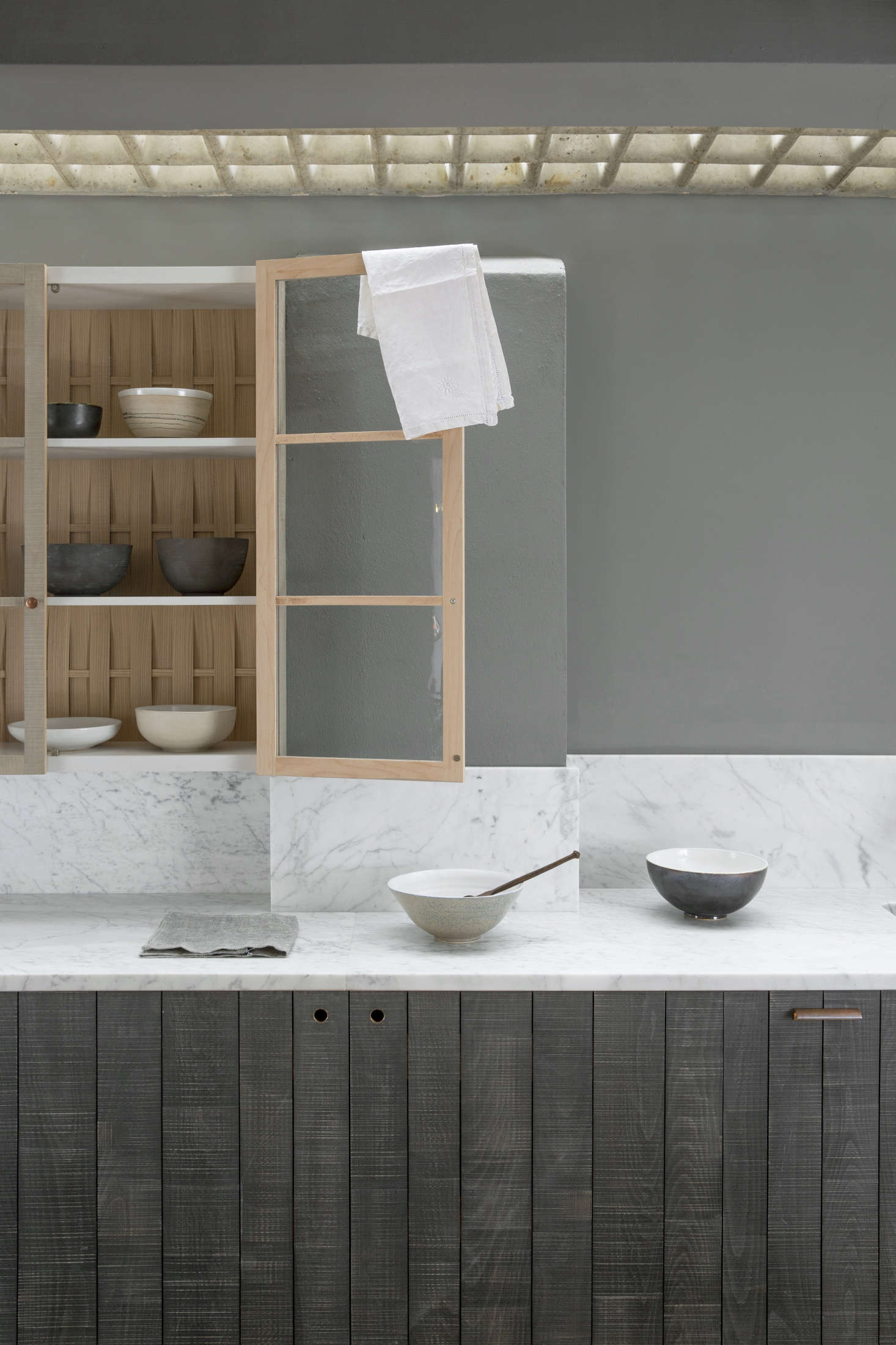 A glazed wall cupboard is detailed with a back of woven wood.