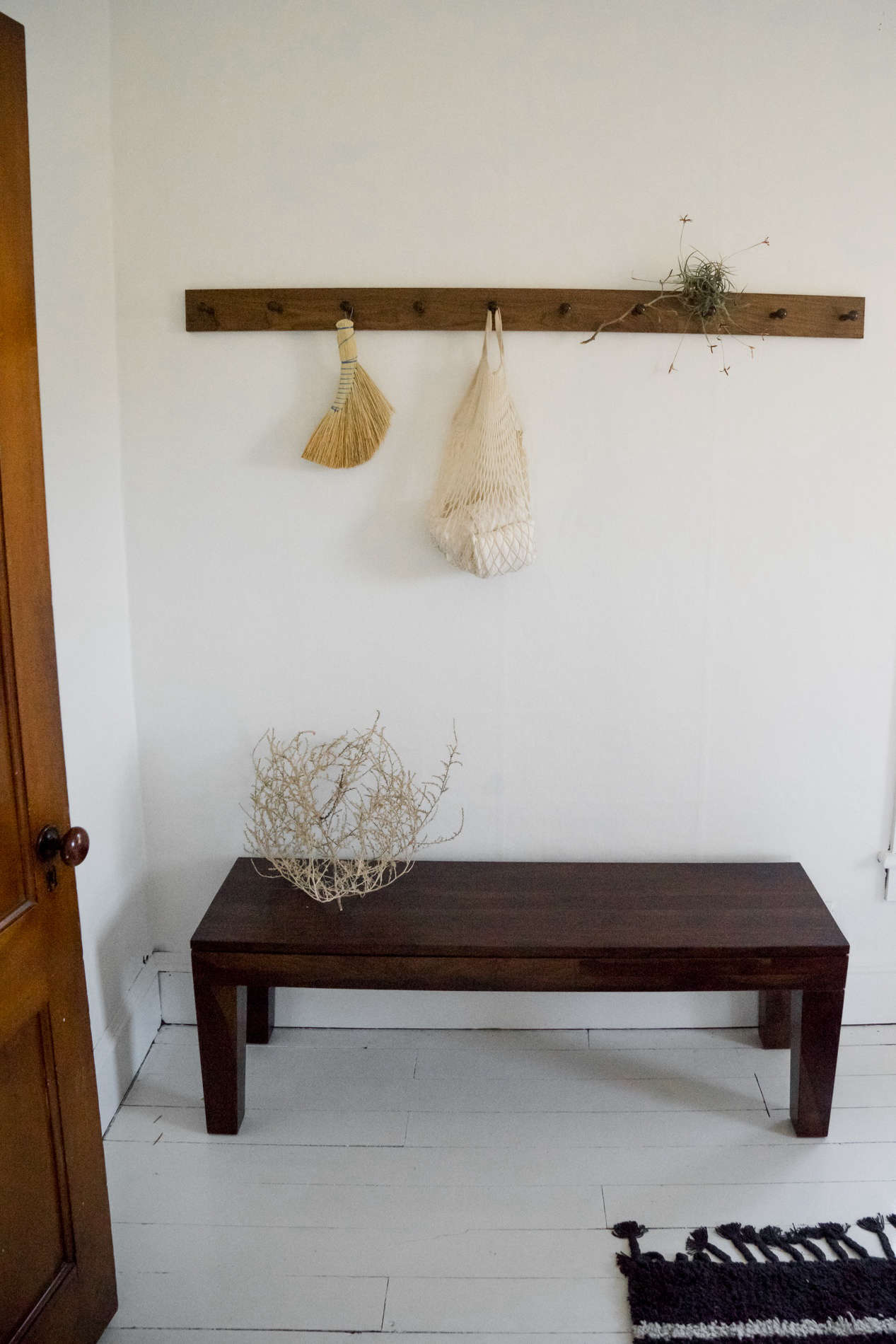 At the foot of the bed, another peg rail holds a Redecker hand broom and dried tumbleweeds.