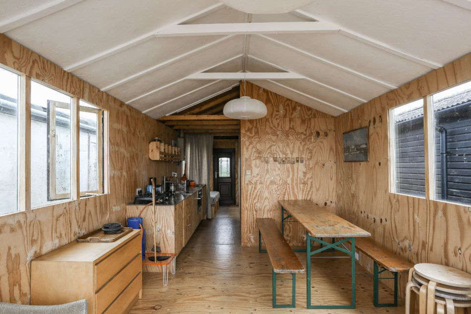 Across from the compact kitchen is a biergarten table and Ikea stools for extra seating. Photograph by Marcia Mihotich from Two London Creatives Shore Up a Tiny Beach House, Ikea Hack Kitchen Included.