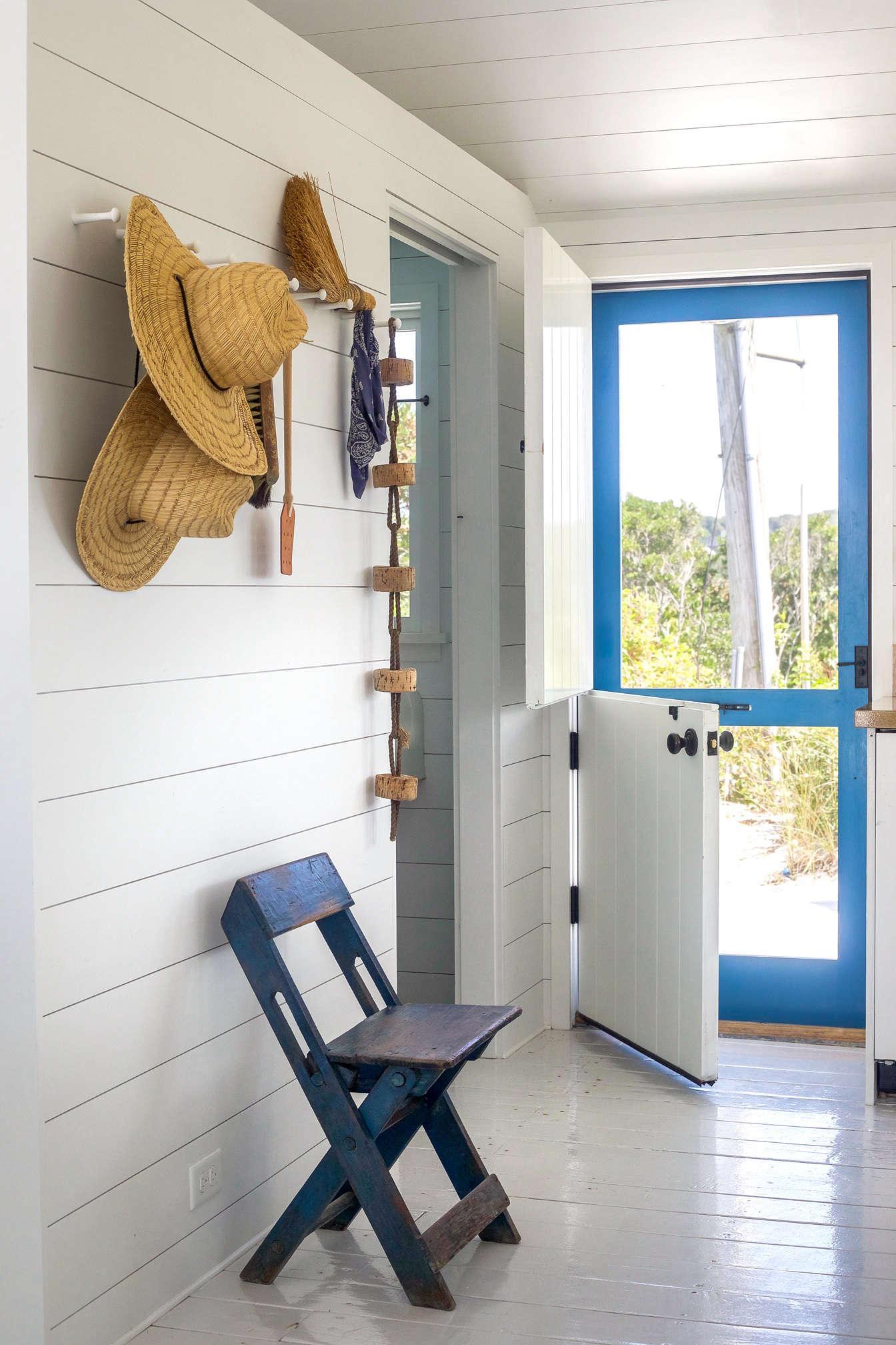A Dutch door ushers in sea breezes (the screen door is painted in Benjamin Moore Blue Macaw high gloss); the cork buoy on the peg rail came with the original house. The floors throughout the house are painted in a California Paint high gloss finish and the interior walls and ceiling are Benjamin Moore PM-
