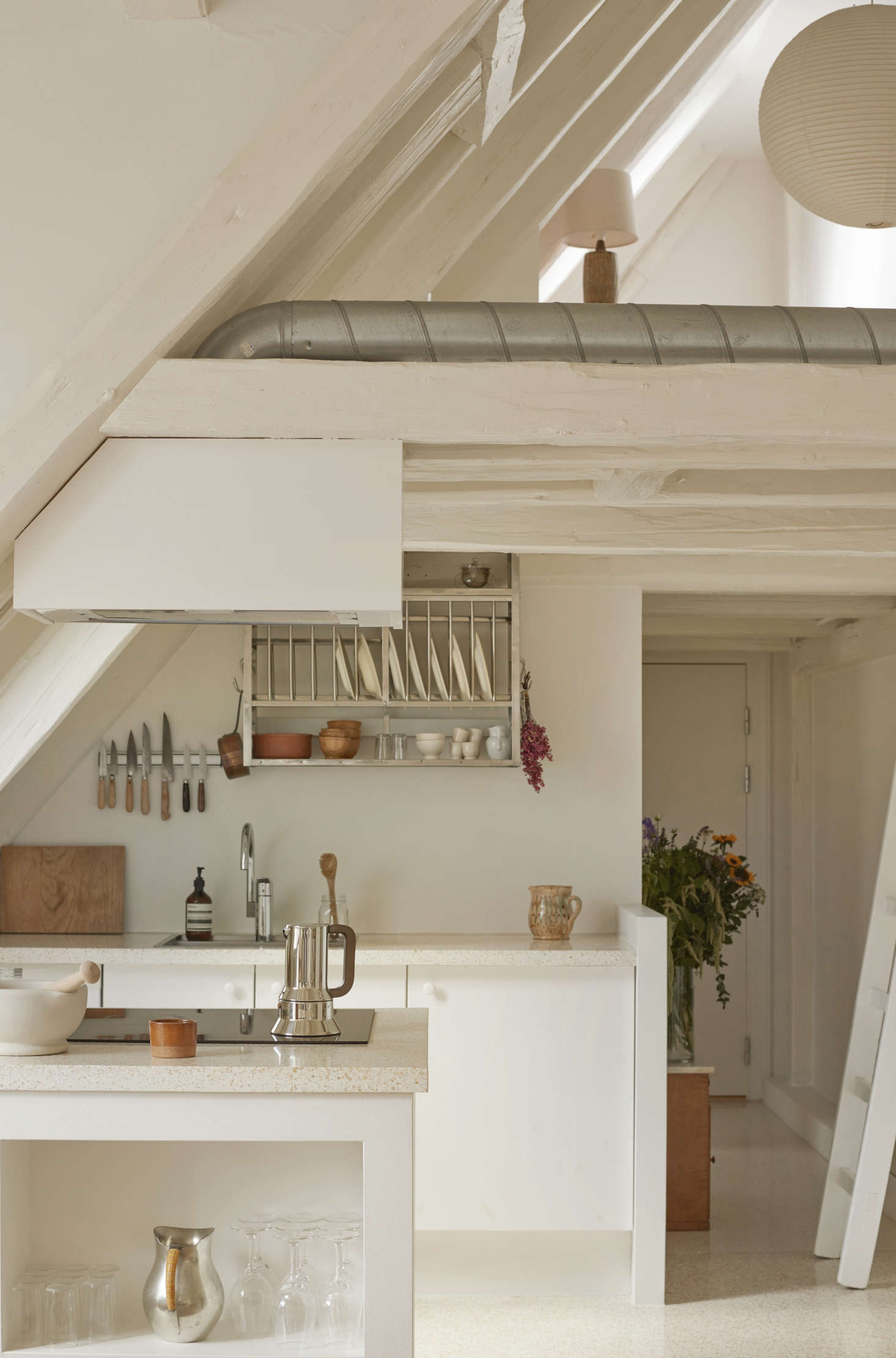 The all-white kitchen sits beneath a lofted home office on the top floor of the historic building. Photograph courtesy of Katrine Rohrberg from Danish Heritage: A Copenhagen Townhouse Renovated by Hand.