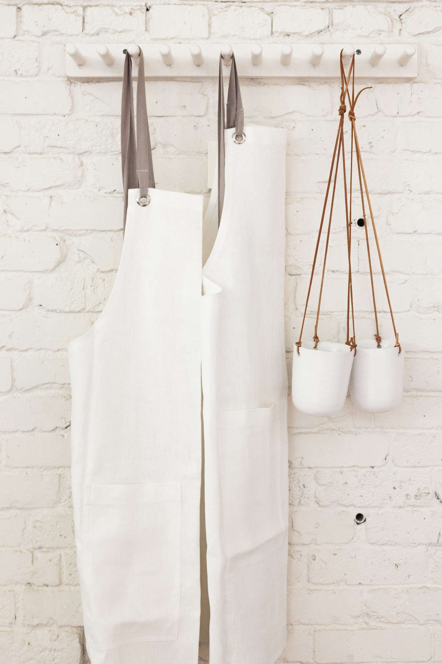 Hanging opposite the retail wall: white linen aprons by Studiopatro and a pair of hanging ceramic planters.