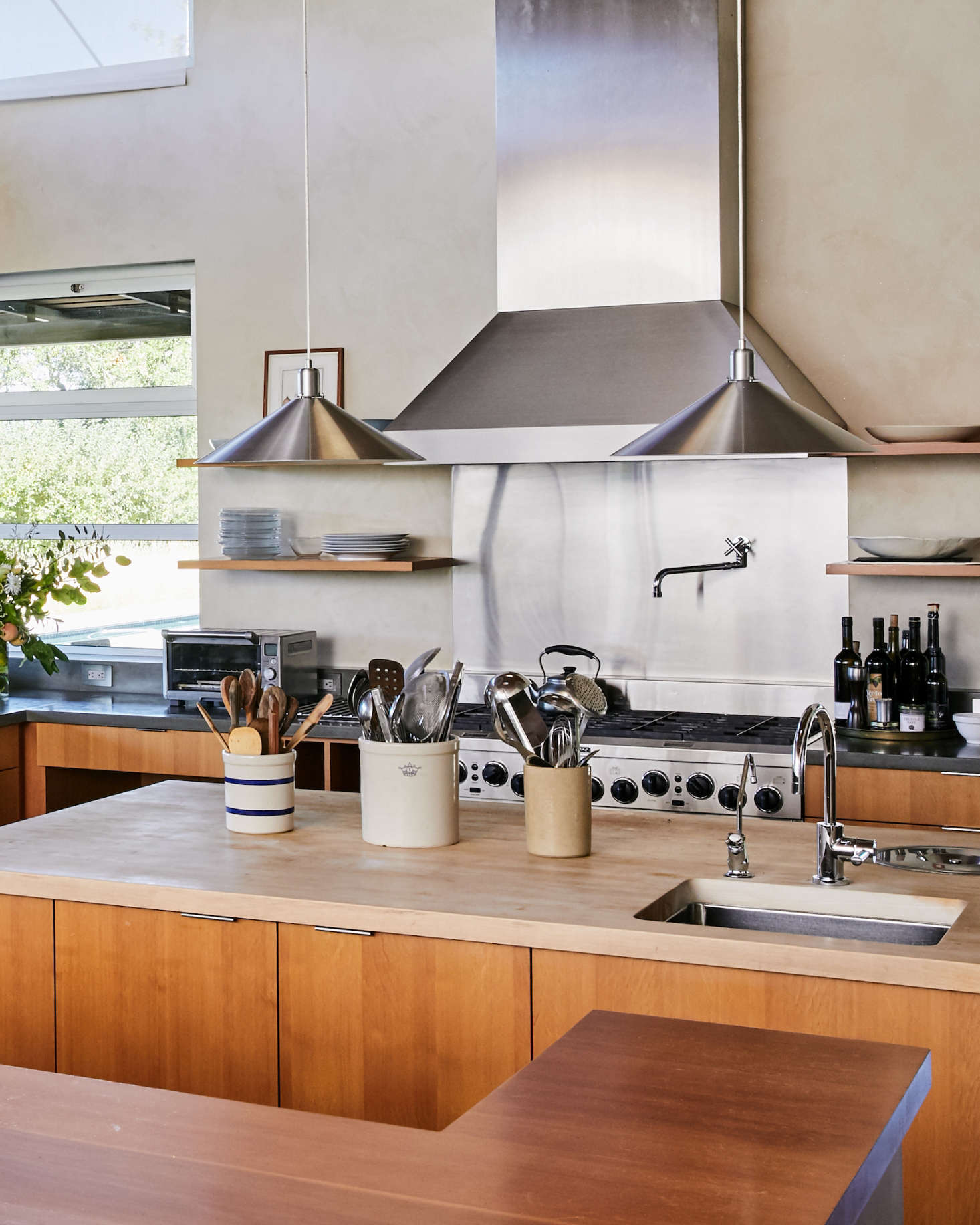 Cooking utensils are stored in stoneware crocks on the island. The custom wood cabinetry is made of vertical-grain Douglas fir, and the kitchen faucets are Dornbracht.