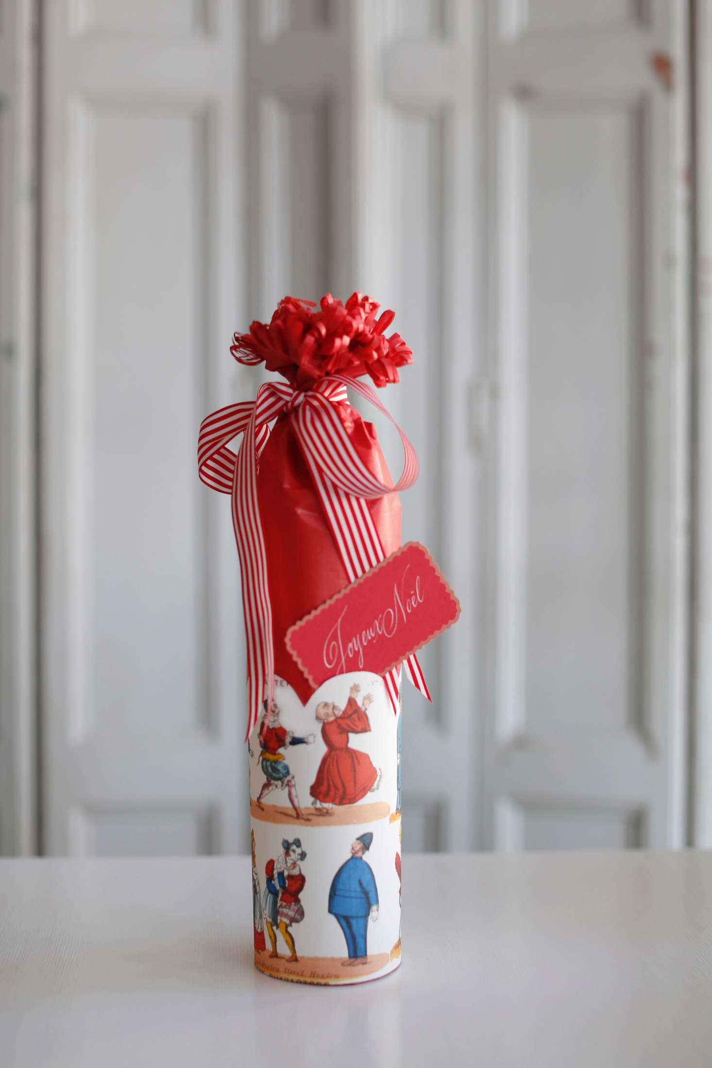 A whimsical presentation for a wine bottle wrapped in tissue paper and topped with a French striped taffeta ribbon, English toy-print paper, and a hand-calligraphed Joyeux Noël card by the shop