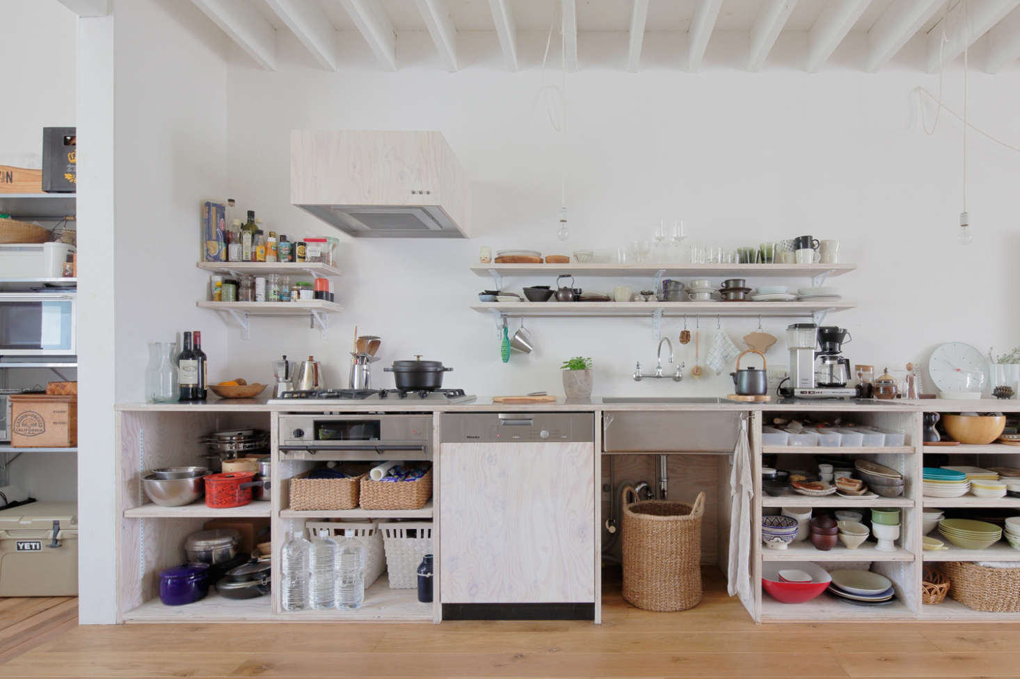 The open kitchen is composed of larch plywood finished with translucent white Osmo Wood Wax—a combination also used for the wall storage, vent cover, and Miele dishwasher panel. The counter is stainless steel and under the cooktop is a shallow fish grill.