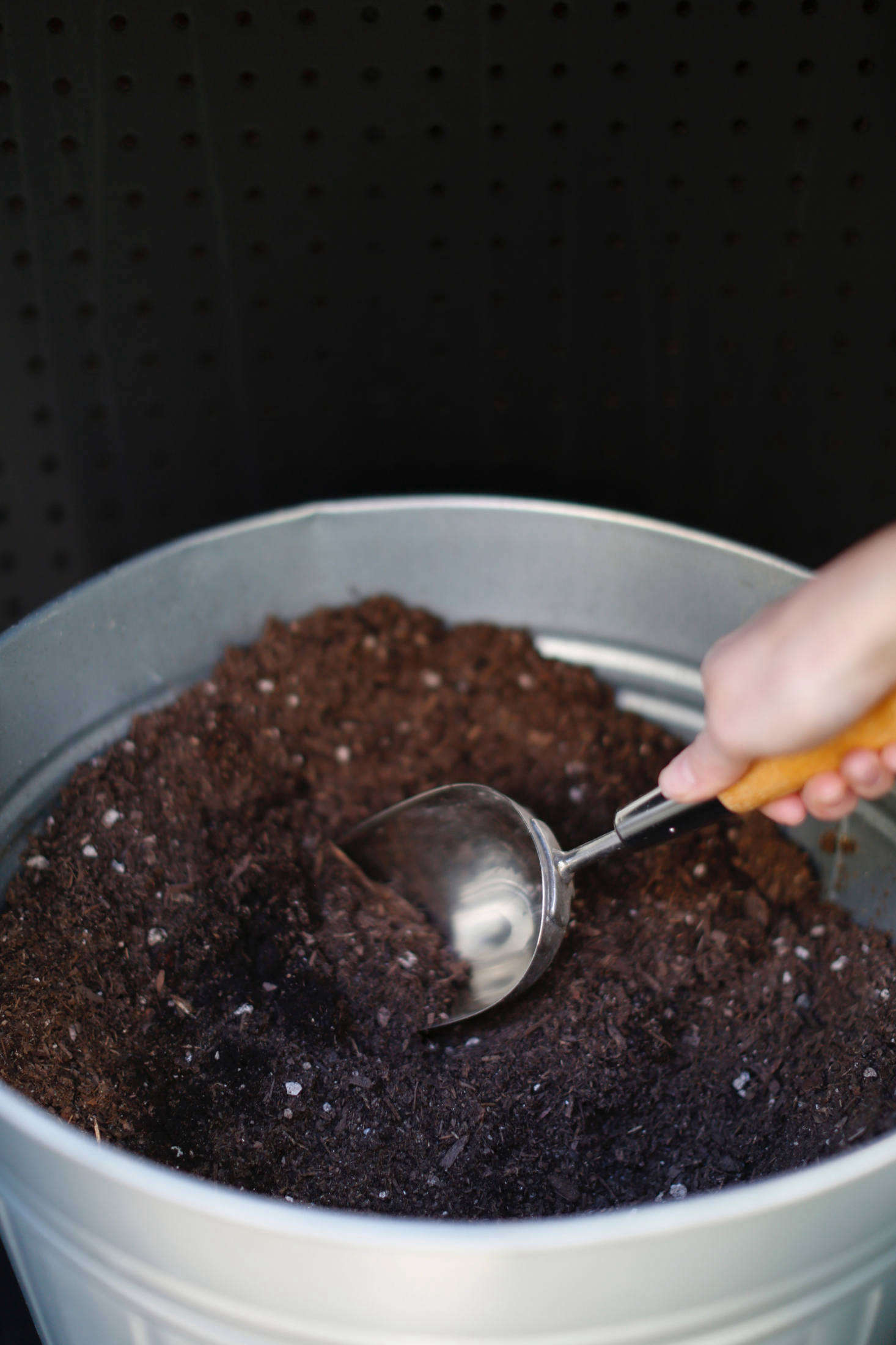 Michelle stores potting soil in a lidded trash bin beneath the shelf. Its scoop hangs on the pegboard when not in use.