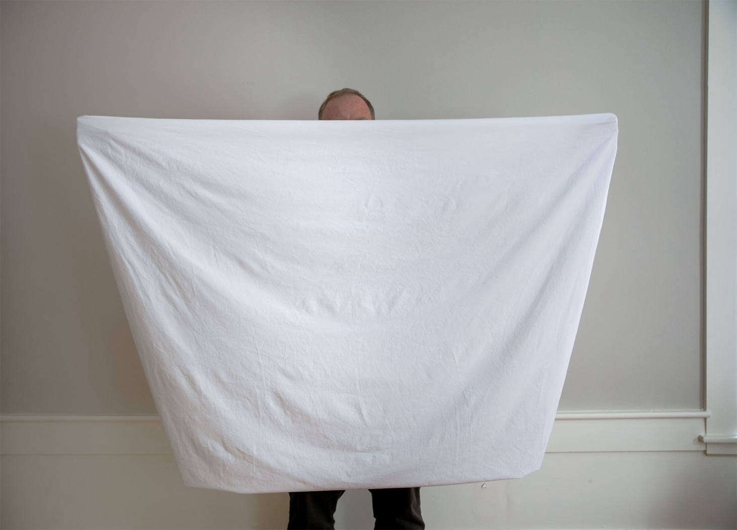 Keeping one hand inside the first corner pocket, run the other hand along the elasticized seam until it reaches the next corner pockets, turning your sheet as you go, and tucking one corner pocket inside the other. The sheet should now be folded in half, with the corner pockets tucked into one another at the top of the sheet, one hand in each.