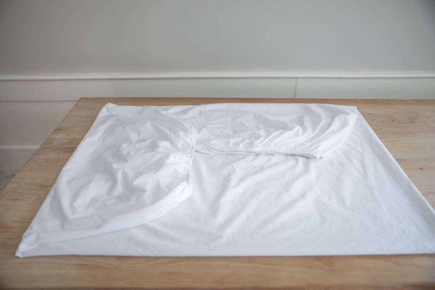 Lay the sheet on a flat surface with the single corner pocket and elastic edges folded over so that the sheet is square. Smooth the sheet. Having eliminated the awkward shape caused by the elastics, you may proceed to fold your sheet as you normally would.