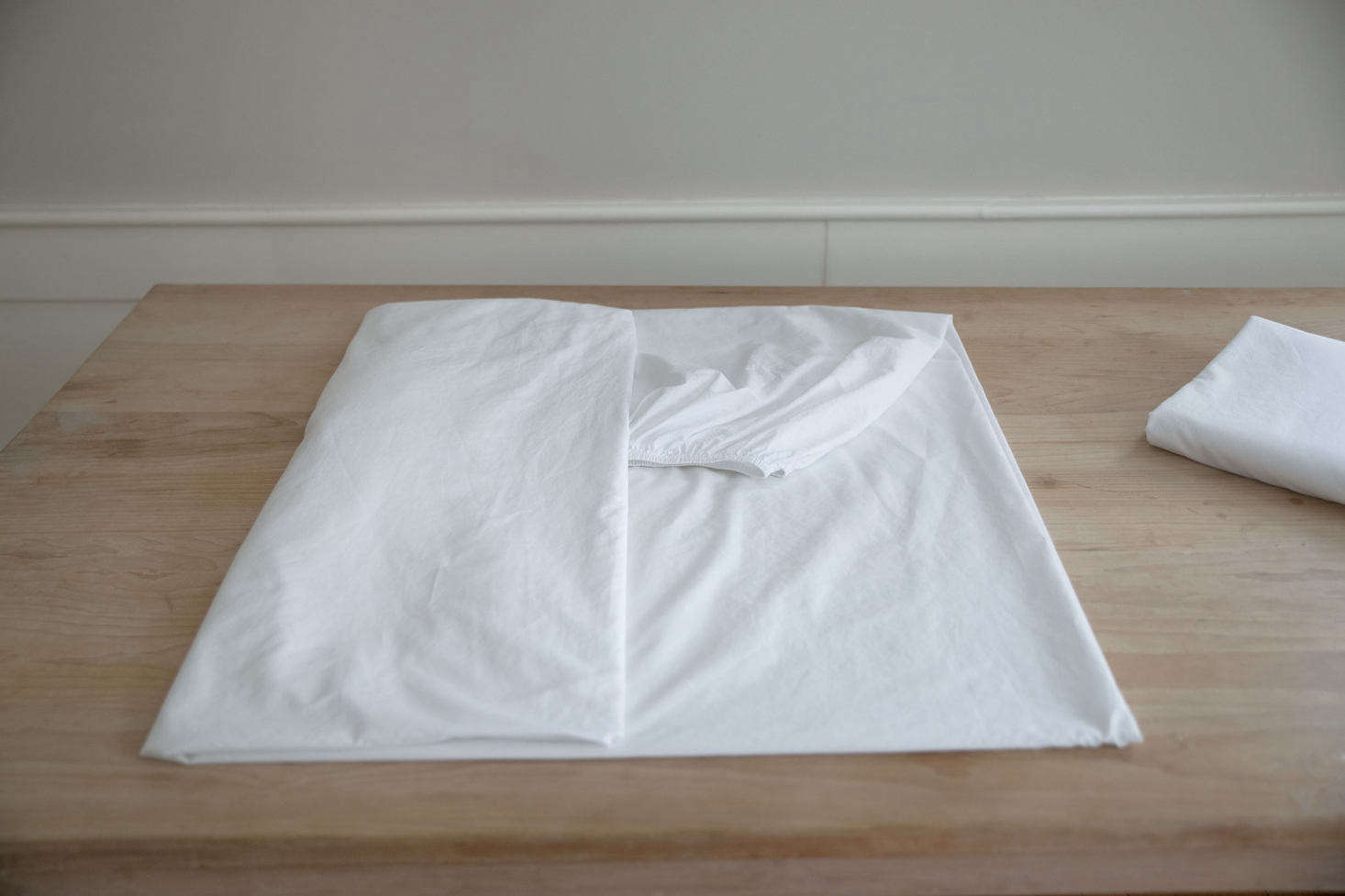 Using a neatly folded flat sheet as a size guide, fold the now-square fitted sheet lengthwise into thirds or quarters.