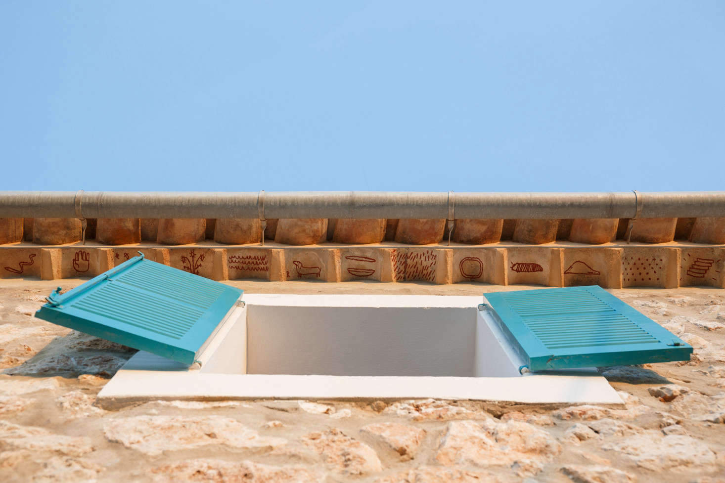 In another nod to Mallorcan tradition, the architects hired artist Luis Urculo to paint small rust-colored symbols beneath the roof tiles—a play on the medieval tradition of teules pintades, said to protect the inhabitants of the house. Of the bright shutters, the architects say, 