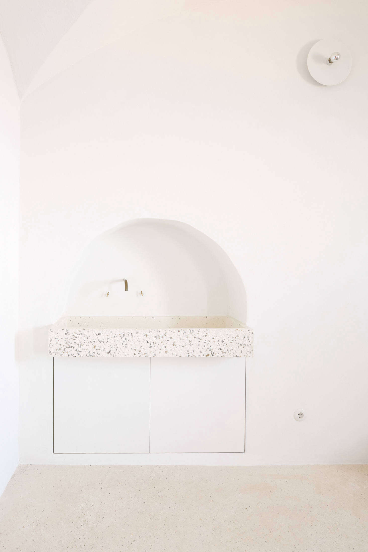 Palencia and Colón preserved a small archway in the kitchen and installed a custom tinted-concrete sink by local company Huguet, a reference to Mallorcan stone sinks. Two cabinets underneath store cleaning products and house the waste bin. Of the subtle white light overhead, the architects say: 