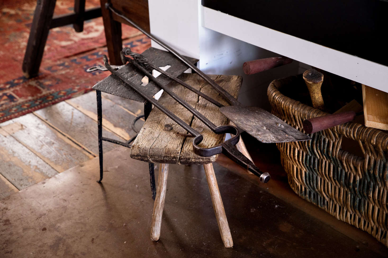 American fireplace tools from the 00s rest on iron standing trivet and an antique stool from Tuscany.