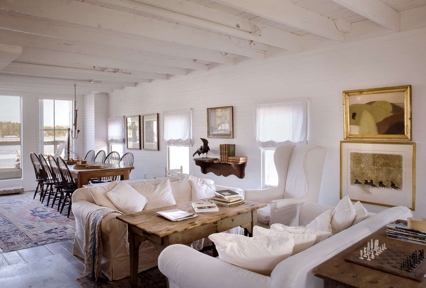 White linen-covered furniture and gold accents give the living room a cozy feel. The top painting on the far right is by an Irish artist, living in Maine. Below is a painting found in France at an antique fair.
