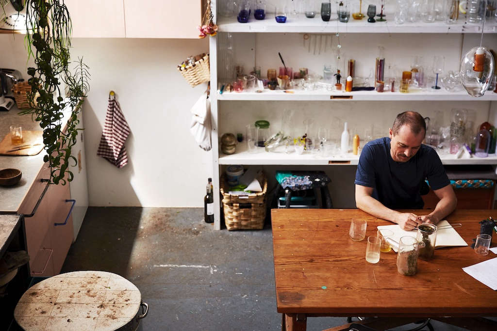 The glassmaker in his kitchen. His workbench can be seen to the left of the kitchen.