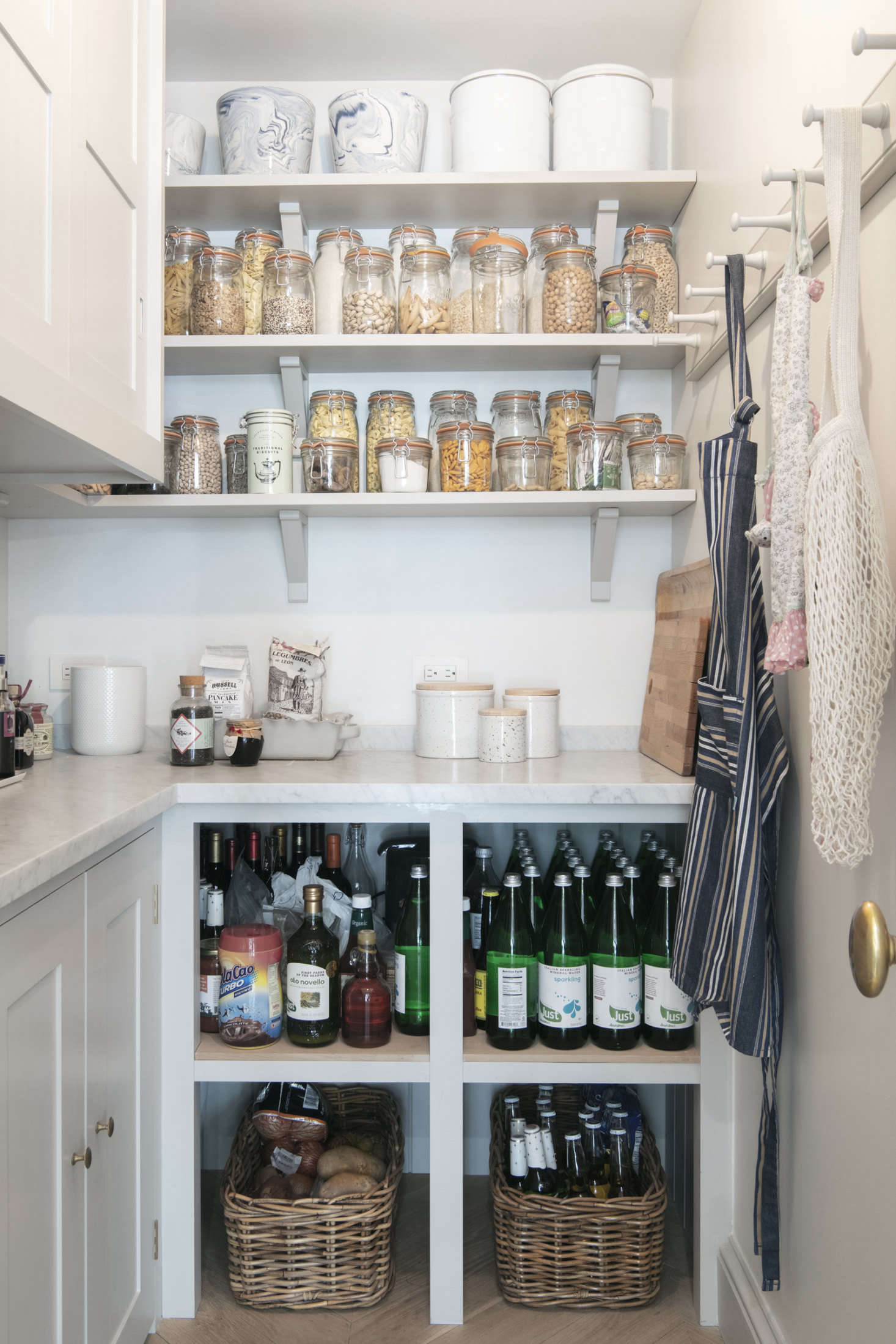 A proper pantry with a marble counter and a peg rail for shopping bags and aprons. Dry goods are decanted into Le Parfait Jars. The upper cabinets hold the microwave and coffee machine; bakeware is stowed in the lower ones.