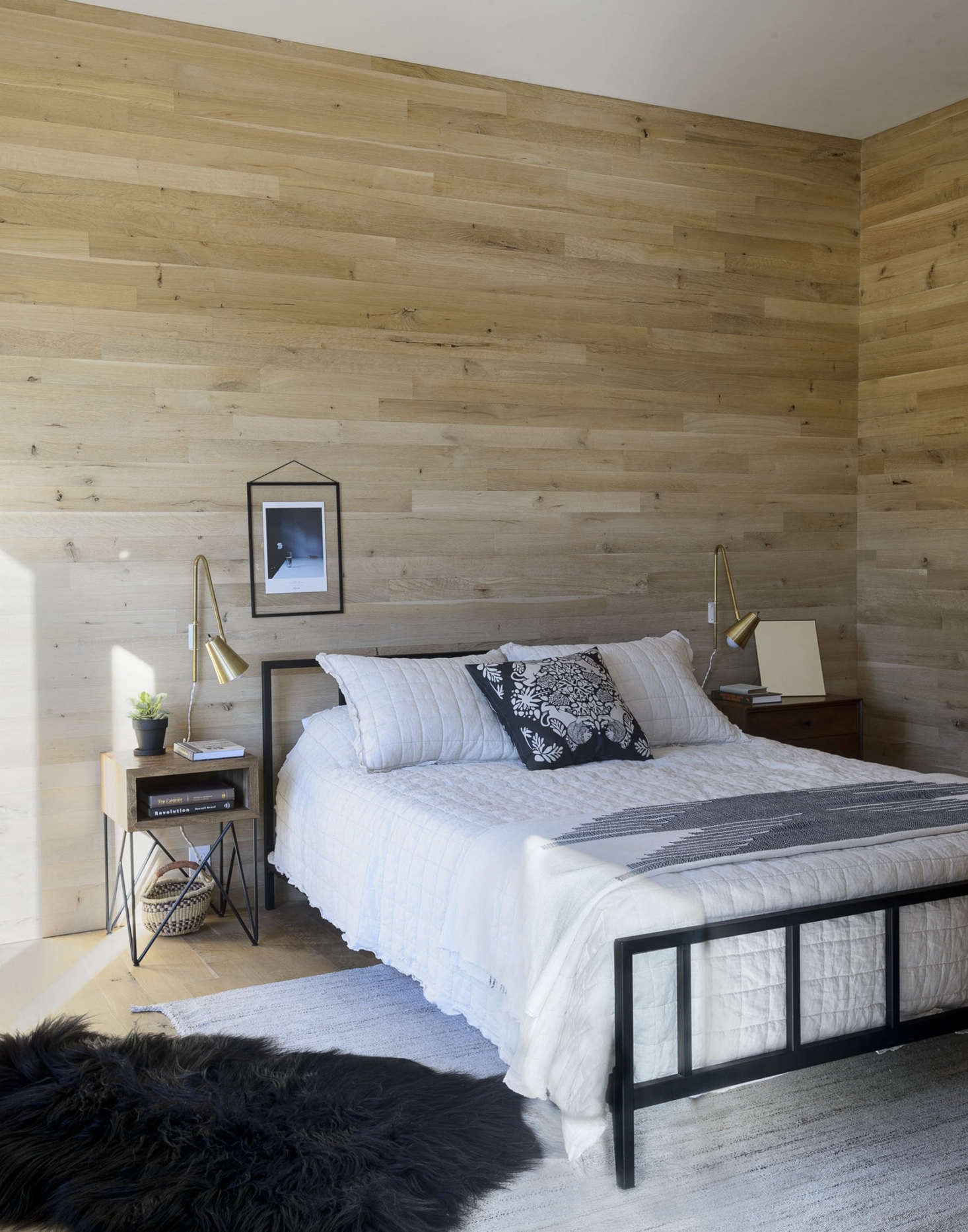 The flooring (and much of the ceilings and walls) is oak. Brass accents can be seen throughout the home, including in the guest bedroom, where brass Wallace sconces by onefortythree flank a black Alchemy bed from CB