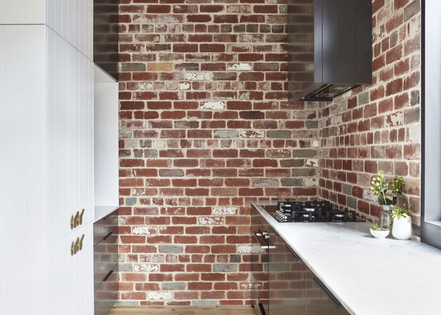 The range is situated at the end of the marble sink counter with an exhaust vent set in a charcoal-painted cabinet. Concealed behind paneled doors, the fridge and freezer are tucked into the extension. All of the appliances are by Fisher & Paykel. The brass fridge/freezer handles are the Como design from Pittella.