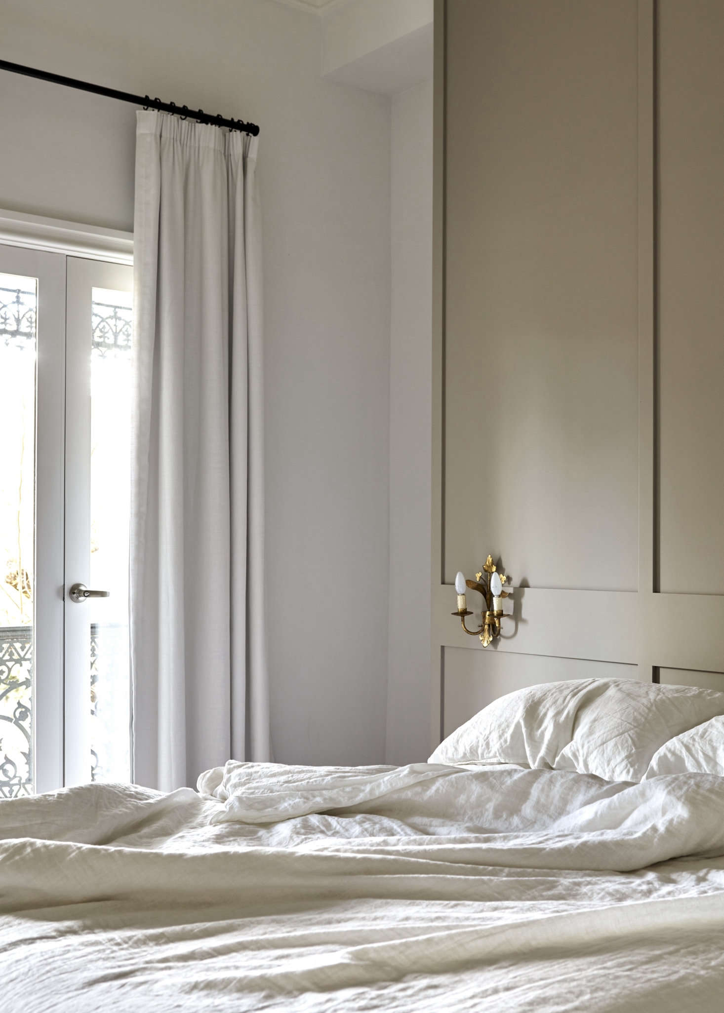 French doors open to the front balcony. Tom and Soma bought the antique sconces on a trip to Paris. The linen bedding is by Bedouin Society.