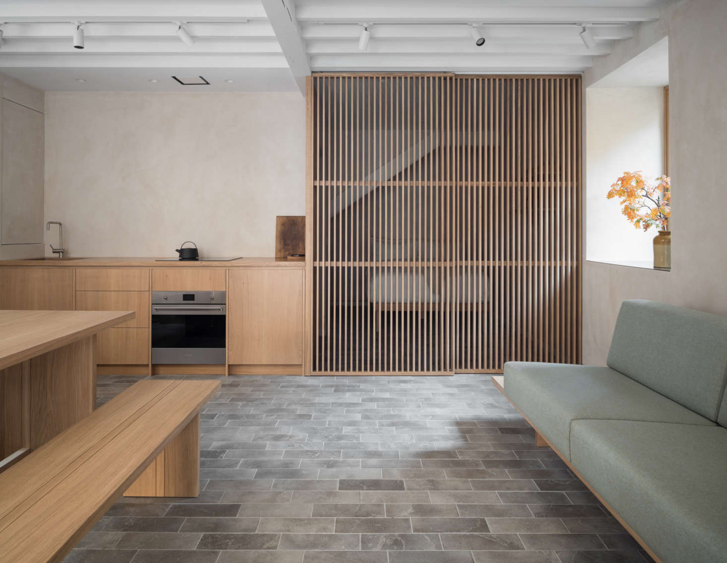 The gray limestone tiles—with radiant floor heating—echo the cobblestones outside. In the back of the room, a second slatted wood screen divides the bedroom from the rest of the quarters.