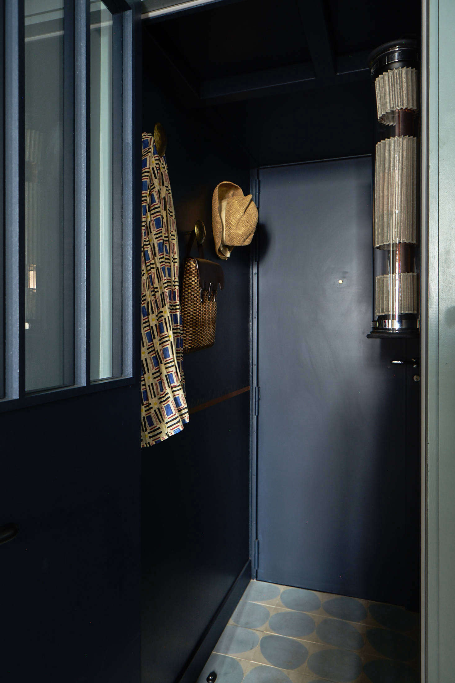 Visitors step into a compact but bold entryway, with dark blue walls, bronze hooks, for corralling and displaying essentials; and—another trademark of Evennou