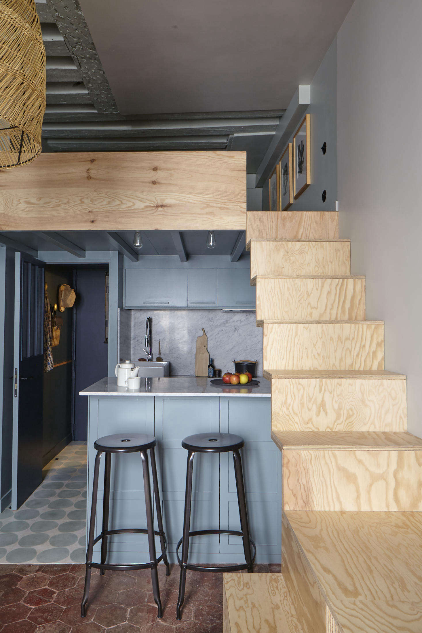 Tucked under the plywood stairs at the back of the apartment is a petite galley kitchen, awash in shades of blue. (The entry is at left, through the blue door.) The mod floor tiles are by Claesson Koivisto Rune via Marrakech Design.