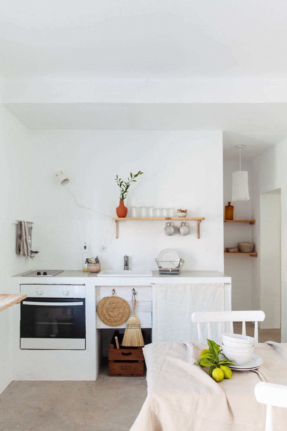 In another simple kitchen, a cabinet is fitted with linen skirt. Also on hand: a hand broom and woven trivet.