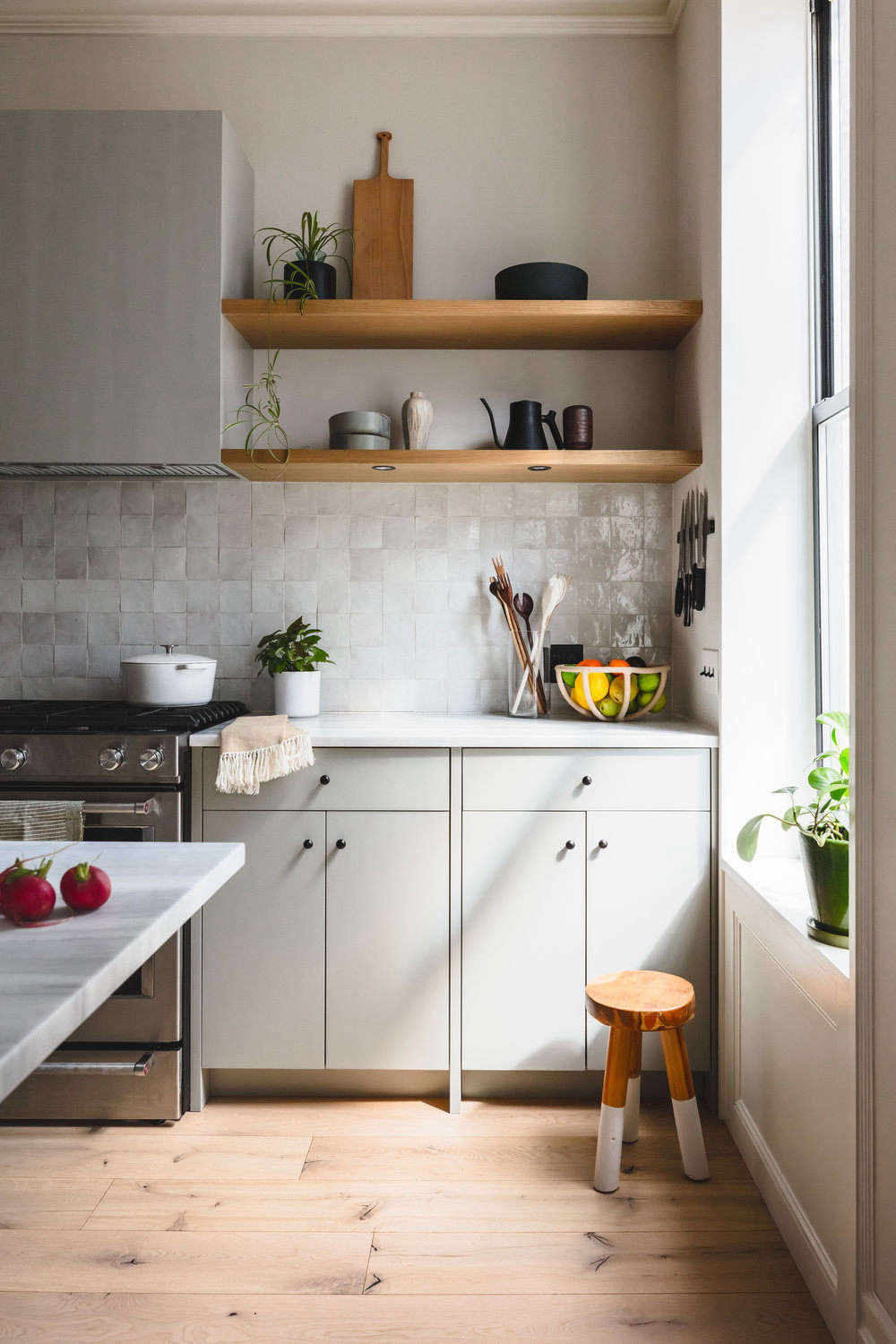 The counter and open shelves are reserved for a few kitchen tools, such as cutting boards and wooden spoons by Allison Samuels of Two Trees Studio and a Terracotta Fruit Bowl by Virginia Sins. Dishes and the couples