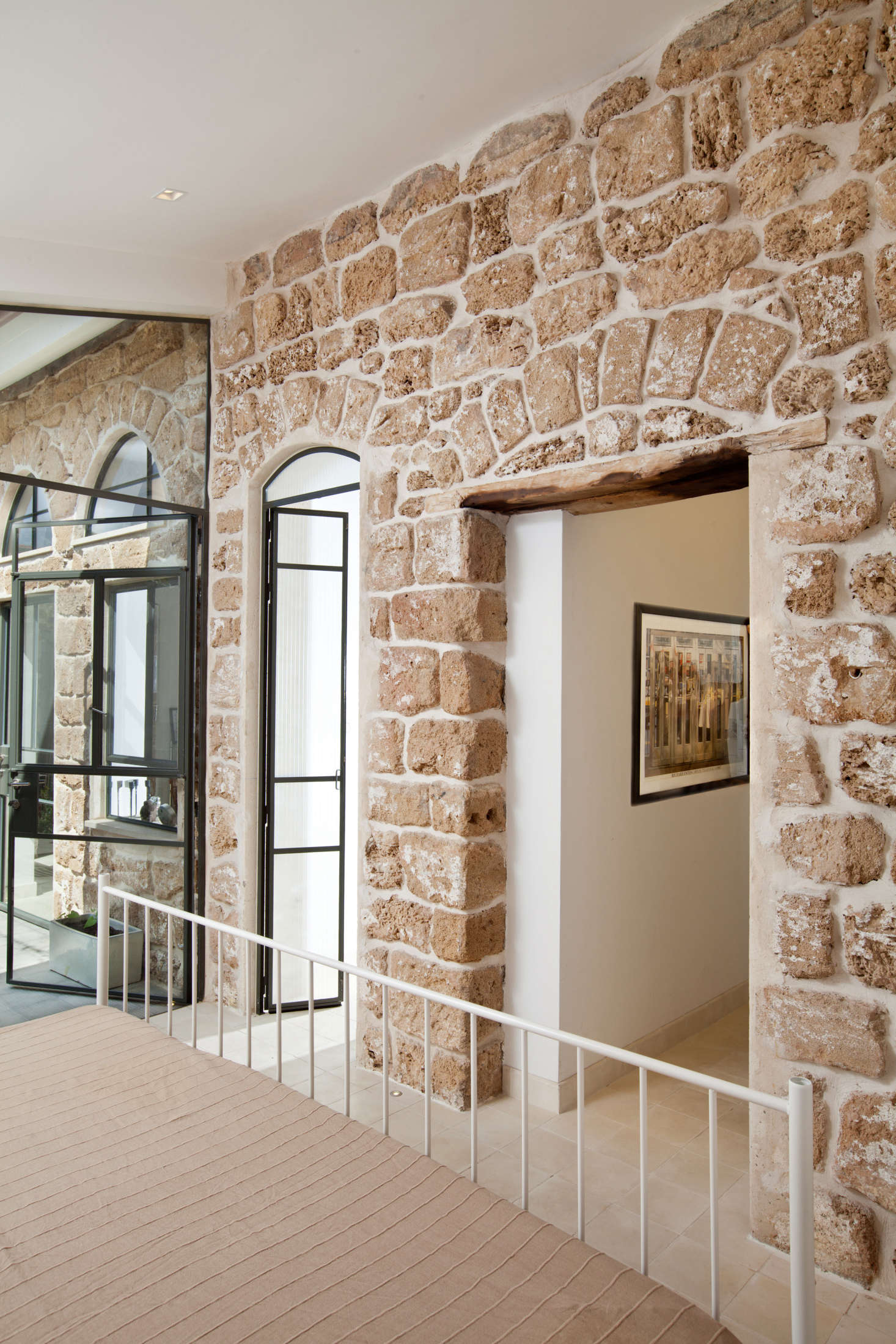 To contrast with the original limestone wall and maintain a feeling of openness, Dvir and Canetti added walls and doors made of glass and steel, like these in the guest bedroom.