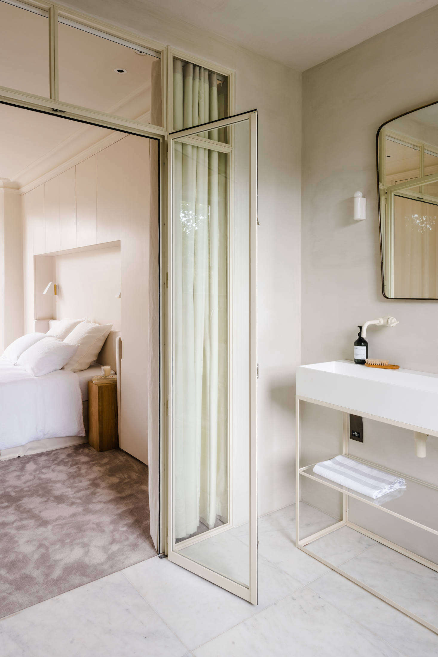 A steel and glass partition separates the bedroom from the bath. The custom vanity unit is from Iusso Stone.