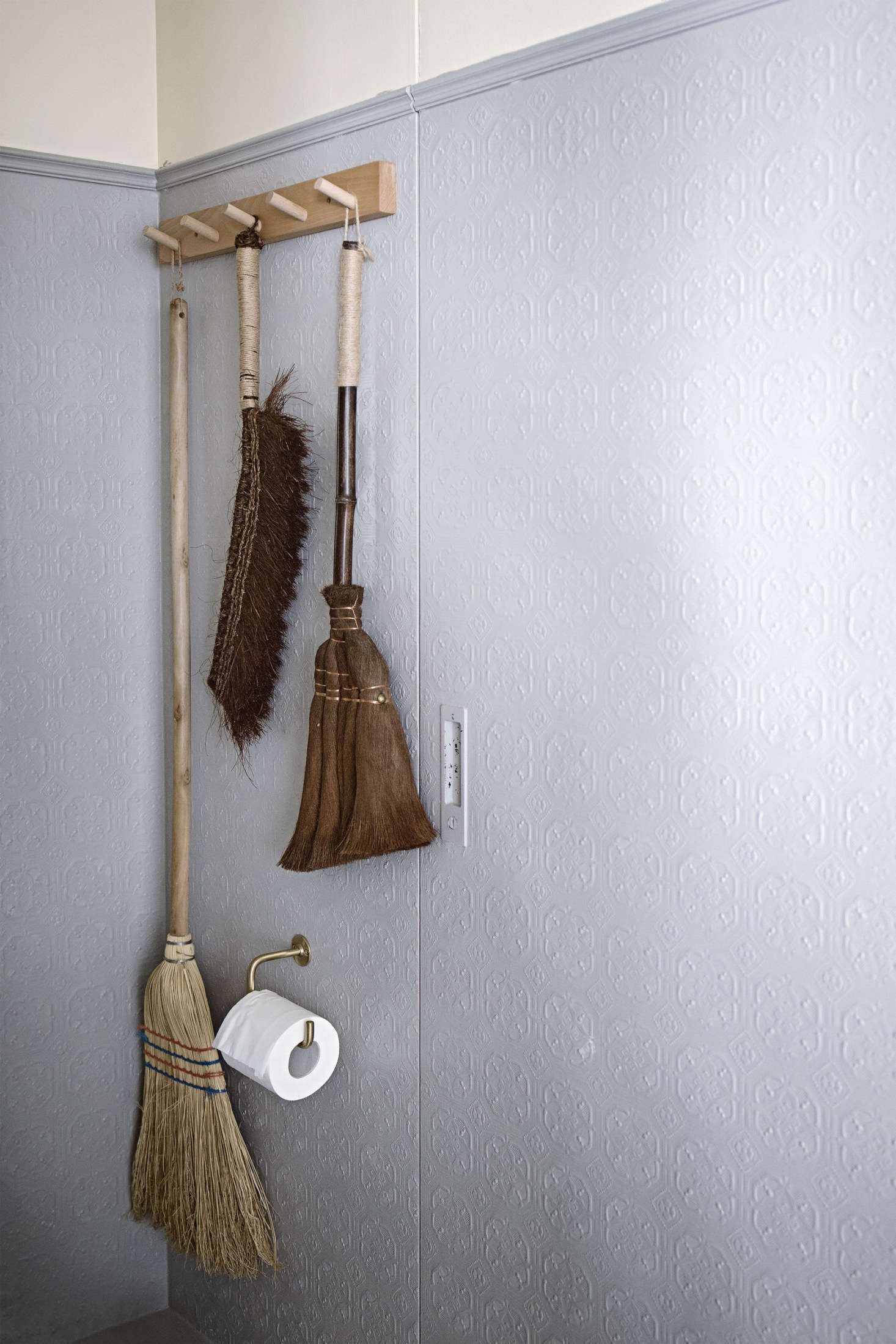The guest bathroom has artful brooms hanging off a peg rail. Painted textured wallpaper lines the walls here. Mandy