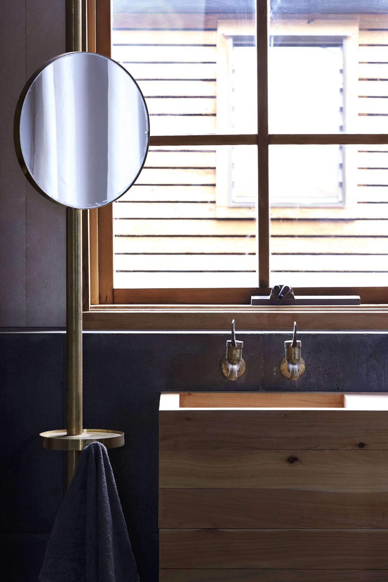 The bathroom has a homemade cypress sink and one of the cypress-framed windows that replaced the existing aluminum ones. The mirror is cleverly positioned on a standing brass valet that also incorporates a small table and towel hook. 