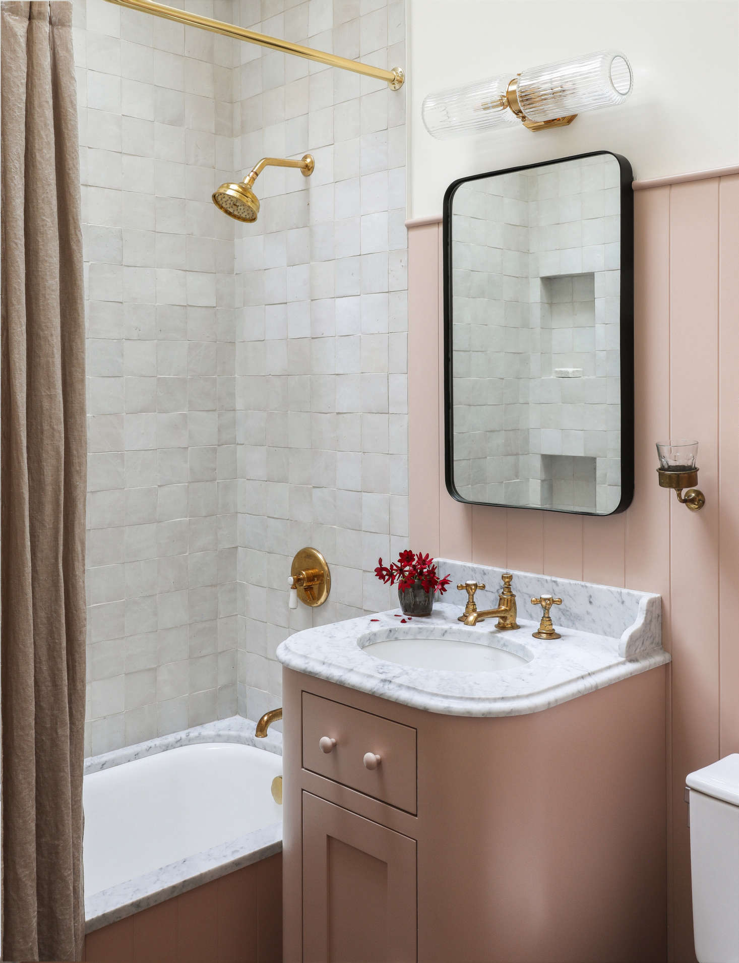 The same vertical paneling applied in the kitchen appears in the overhauled tiny main bath, where a custom pink vanity stands alongside a five-foot-long tub, all painted Farrow & Ball Setting Plaster. 
