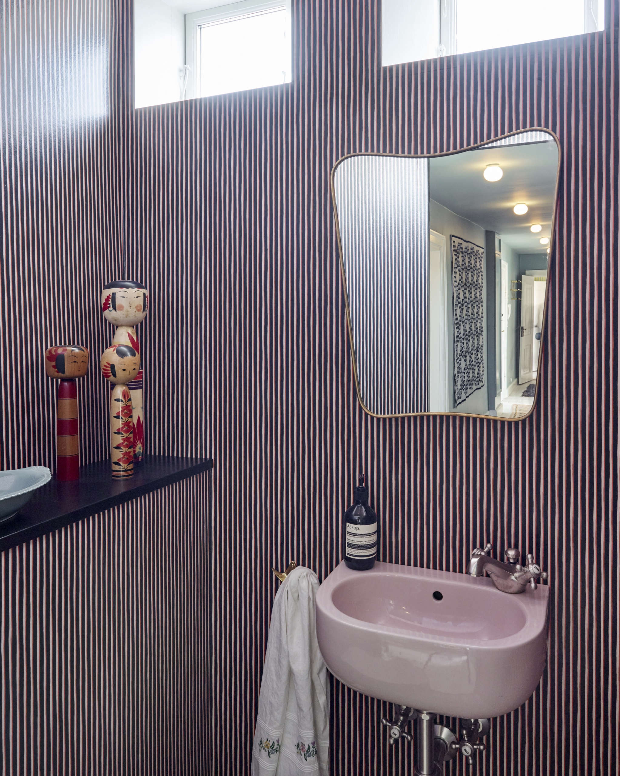 The pretty-in-pink powder room. The Painted Stripe wallpaper—black, orange, and pink—is another Tapet Cafe design. The Brass Mirror is a Gio Ponti classic from the 50s available from The Apartment (