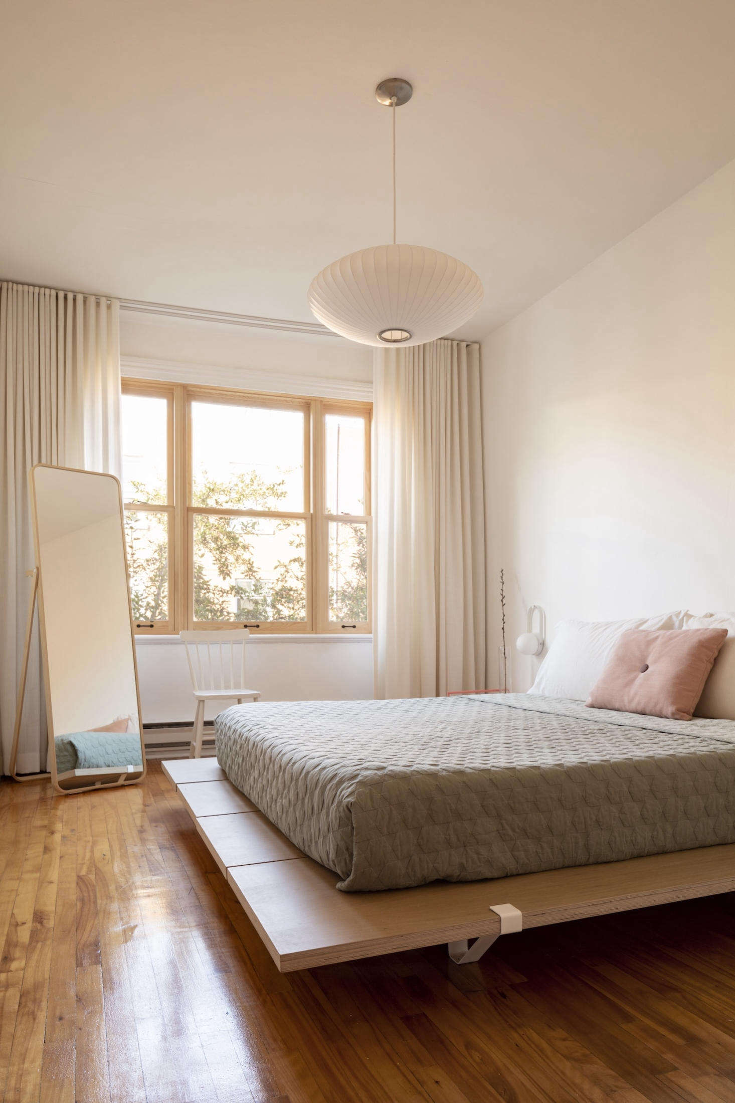 The third floor has two bedrooms. Here, simplicity abounds. A Nelson bubble lamp hangs above a platform bed from Floyd. The mirror is from Ikea.