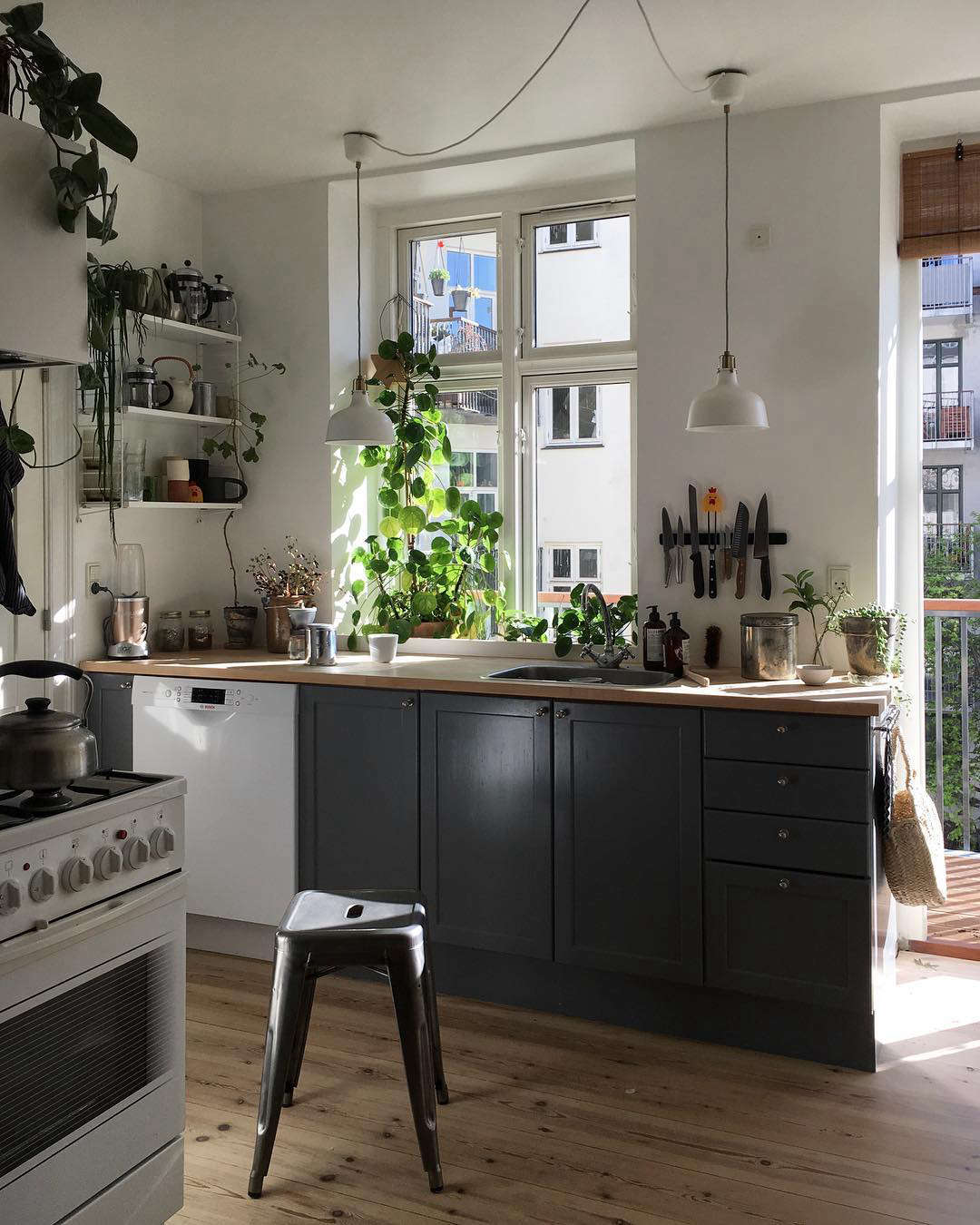 The small and sunny kitchen, with plain wood floors, butcher-block countertops, a newly installed balcony, and plenty of houseplants. 