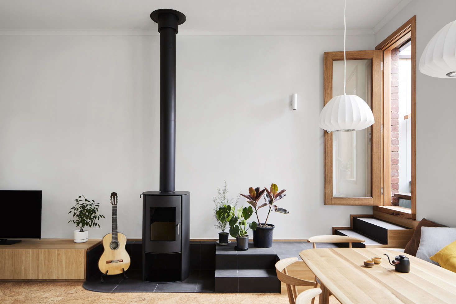 Just beyond the living room is the dining area, over which hangs two Pluto Pendant lights from About Space. The fireplace surround and steps leading to the roof deck are tiled with bluestone.