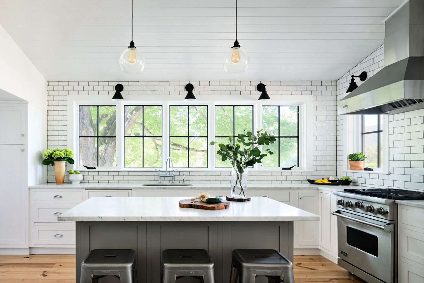 Porter set off the kitchen with subway-tiled walls and a Carrara marble-topped breakfast counter. In lieu of upper cabinets, five windows frame views of an old maple tree.