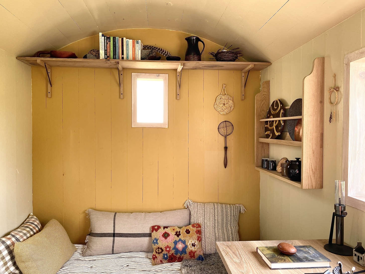 The sofa is a camp cot piled with mattresses, blankets, and pillows. The back wall introduces a bit of color to the room, which is lit by candles and Oil Lamps by Castor.