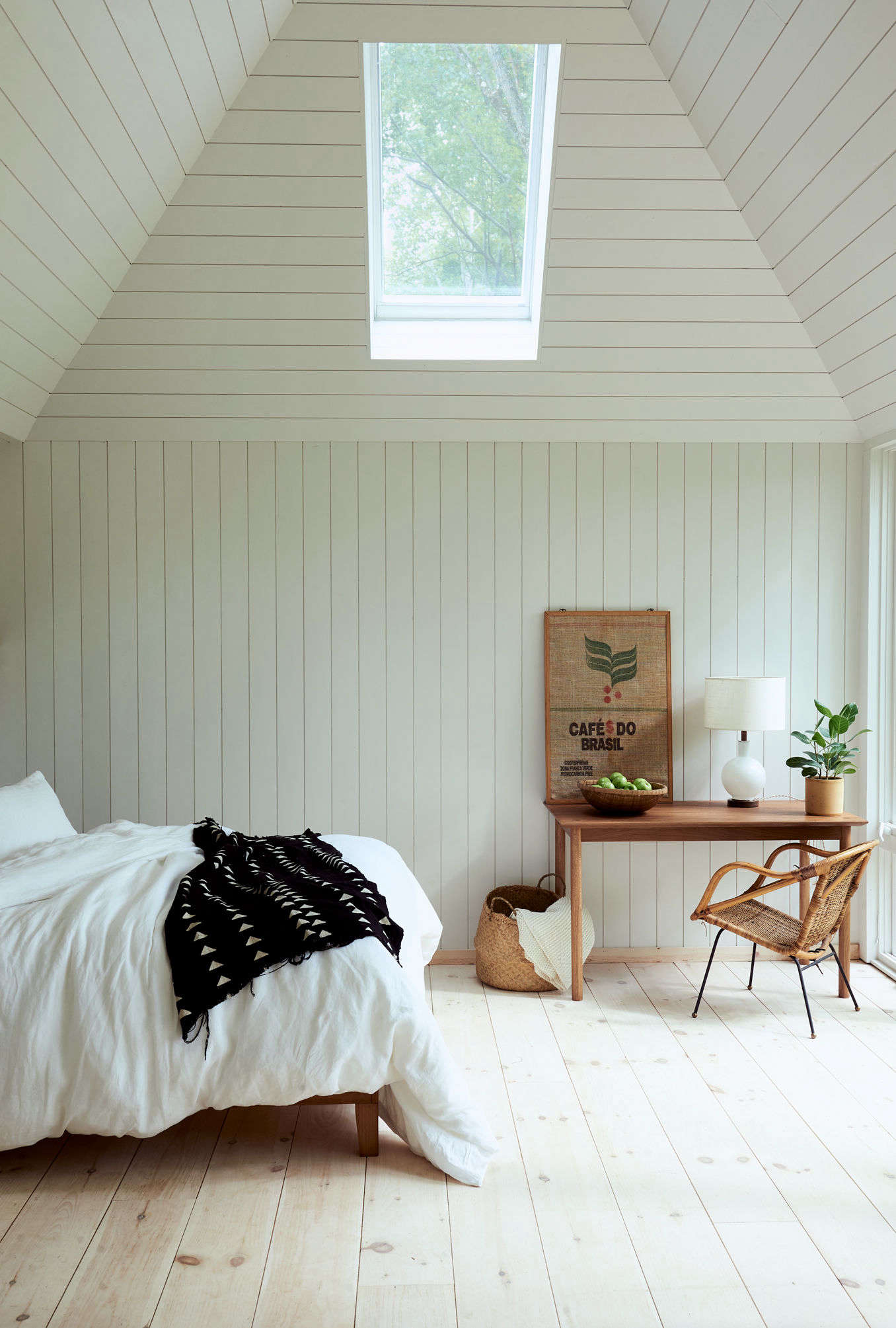 The sole bedroom enjoys plenty of natural light thanks to a skylight and a wall of floor-to-ceiling windows. A vintage wicker chair and a table by Sun at Six anchor one corner.