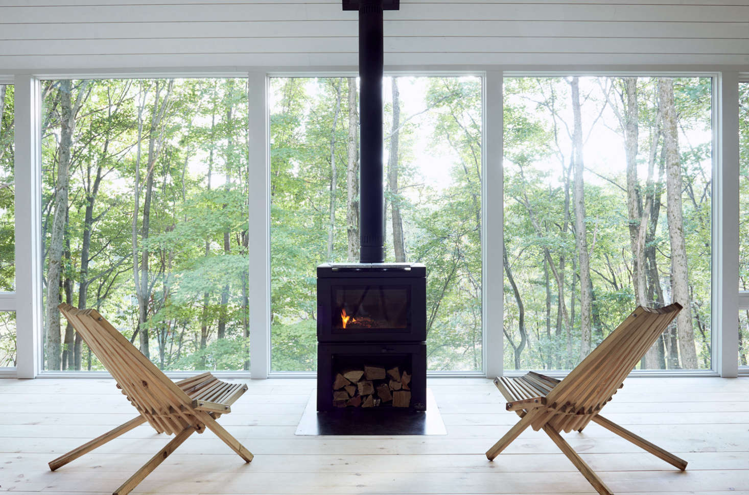 Two vintage Kentucky stick chairs (sourced on Etsy) are situated for optimal forest bathing: in front of floor-to-ceiling Andersen windows and an Osburn Matrix wood stove.