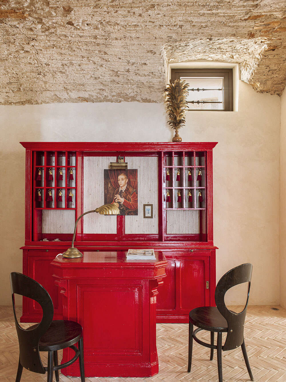 Just add red lacquer: the front desk was created from two flea market pieces renewed with glossy paint and key slots added by a local carpenter. The surfaces here range from newly laid herringbone brick (handmade in Spain) to freshly plastered walls and a ceiling preserved in its excavated state. The chairs are 60s French: the Mouette design from Baumann.